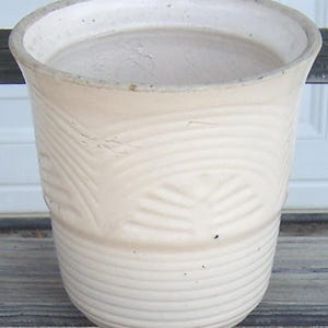 May include: Off-white ceramic planter with a textured, ridged design. The planter has a wide opening and a slightly flared rim. The exterior features a repeating pattern of curved lines and leaf-like impressions, adding visual interest to the piece.