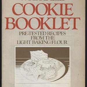May include: A vintage cookbook cover with the title "White Lily Cookie Booklet" in large red letters. The cover features an illustration of cookies on a plate and the text "Pre-Tested Recipes From The Light Baking Flour". The background has vertical stripes.