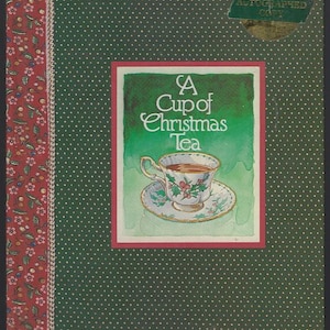 May include: A book cover with a green background dotted with white circles. The cover features a watercolor illustration of a teacup and saucer with holly. The title reads "A Cup of Christmas Tea" by Tom Hegg, illustrated by Warren Hanson.