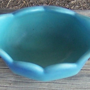 K&ouml;nnte beinhalten: Eine tealblaue Keramikschale mit einem gewellten Rand. Die Schale ist leer und hat eine glatte, gl&auml;nzende Oberfl&auml;che.
