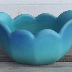 May include: A light blue ceramic bowl with a scalloped edge. The bowl is made in a tulip shape.
