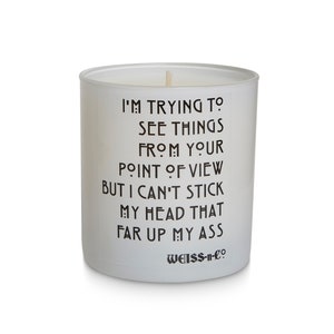 May include: A white glass candle with black text that reads "I'M TRYING TO SEE THINGS FROM YOUR POINT OF VIEW BUT I CAN'T STICK MY HEAD THAT FAR UP MY ASS." The candle has a wooden wick and the brand name "WEISS-n-co" at the bottom.