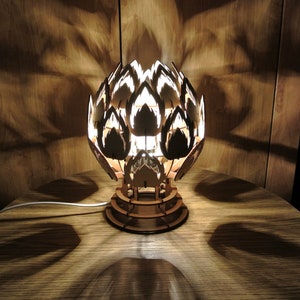 May include: A wooden table lamp shaped like a flower with a light bulb inside. The lamp is on a wooden table and is casting shadows on the surface.