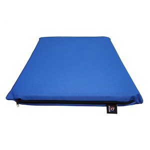 May include: A rectangular blue cushion with a black zipper closure along one edge. A small black tag with white text is attached to the cushion. The cushion is made of a solid blue fabric.