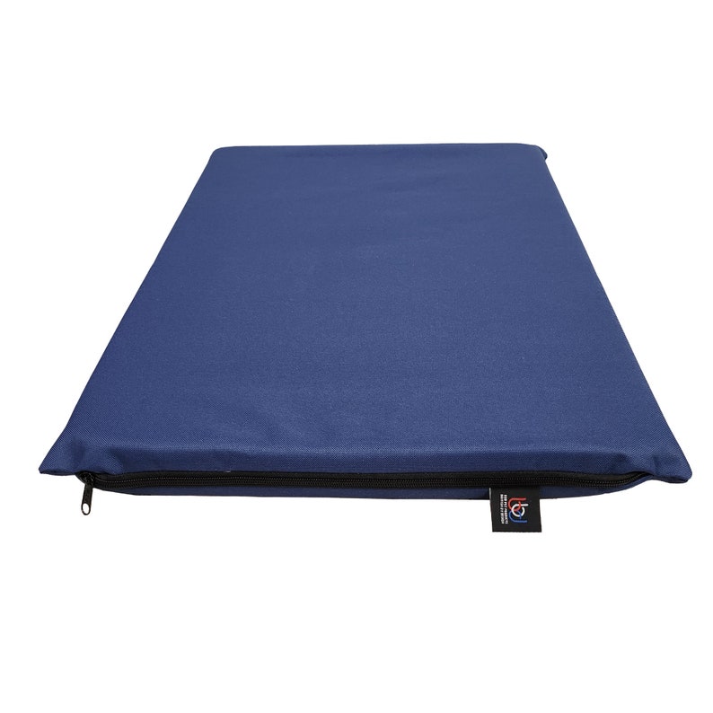 May include: A rectangular, navy blue cushion with a black zipper closure along one edge. A small black tag with white text is attached to the cushion. The cushion is made of a smooth fabric.