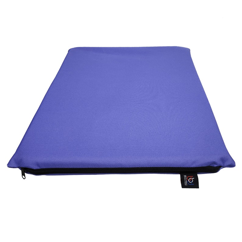 May include: A rectangular, periwinkle-colored cushion with a black zipper along one edge. The cushion has a smooth, solid surface and a small tag on the lower right corner.