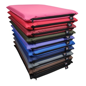 May include: A pile of rectangular cushions in a range of colours: pink, red, green, blue, and brown. Each cushion features a black zip and a small tag. The cushions seem to be made of a durable, water-resistant material.