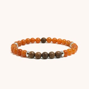 Pode incluir: Uma pulseira de contas com contas laranja e castanhas. A pulseira tem uma mistura de contas redondas de cor laranja e contas de madeira castanha mais escuras. Acentos metálicos prateados separam os diferentes tipos de contas. A pulseira é exibida em um fundo branco.