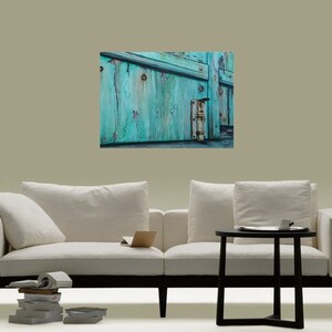 May include: A close-up of a weathered turquoise wooden door with a rusty metal hinge. The door is slightly ajar, revealing a glimpse of the interior.