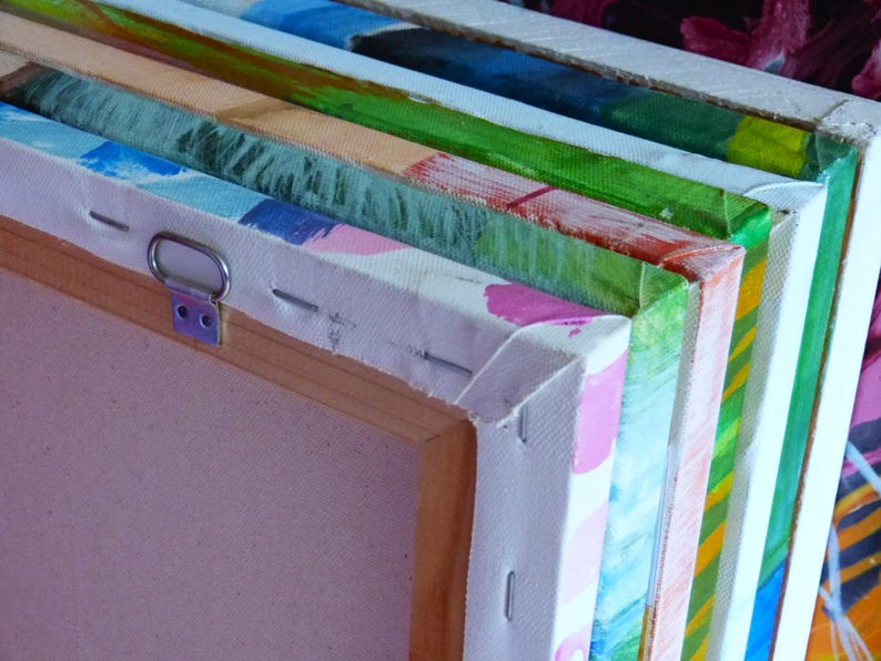 May include: Close-up of the edge of a stack of canvases, showing the wooden frames and the stretched canvas. The canvases are painted in various colors, including green, blue, pink, and yellow.