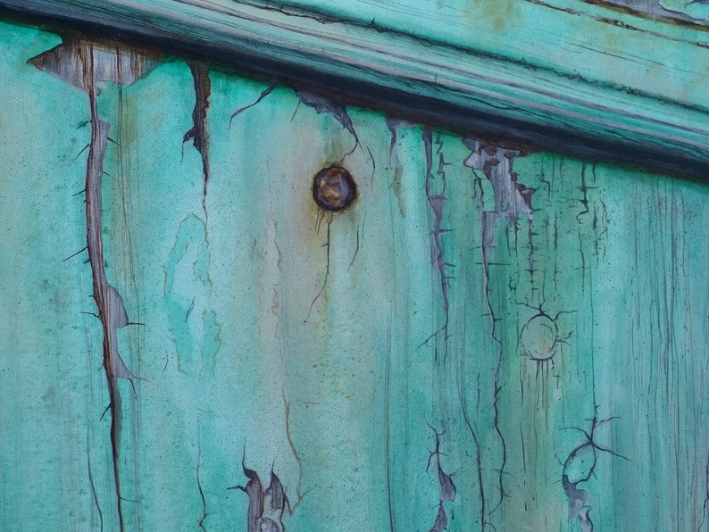 May include: Close-up of a weathered wooden surface painted in a teal green color. The paint is cracked and peeling, revealing the wood underneath. There is a rusty nail head in the center of the image.