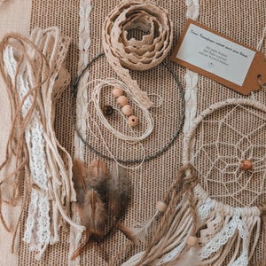 Peut inclure: Un kit de fabrication d'attrape-rêves comprenant un cercle en métal, du ruban en dentelle beige, de la ficelle naturelle, des perles en bois et des plumes brunes. Une étiquette avec du texte allemand et un attrape-rêves partiellement tissé.