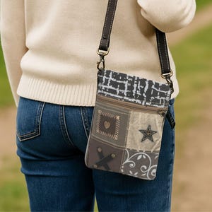 Könnte beinhalten: Eine Patchwork-Umhängetasche mit braunem Lederriemen. Die Tasche hat Stoffquadrate in Braun-, Grau- und Beigetönen mit dekorativen Elementen wie Herz, Stern und floralem Muster. Sie hat einen Reißverschluss.