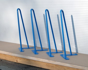 May include: Four blue metal hairpin legs for furniture. The legs are in a row on a wooden surface.