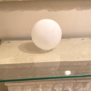May include: A white glass globe sits on a light beige stone surface.