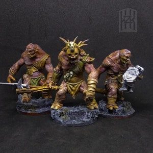 Puede incluir: Tres miniaturas pintadas de figuras humanoides con piel marrón, que llevan taparrabos y sostienen armas. Las figuras están de pie sobre bases negras.