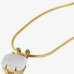Könnte beinhalten: Eine goldfarbene Halskette mit einer dünnen Schlangenkette und einem quadratischen, durchscheinenden weißen Steinanhänger, der von vier goldfarbenen Krappen gehalten wird. Der Anhänger hat eine glatte, polierte Oberfläche.
