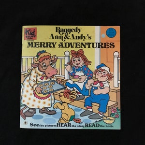 May include: A vintage children's book titled "Raggedy Ann & Andy's Merry Adventures." The cover features illustrations of Raggedy Ann, Raggedy Andy, a cow, and a yellow dog. The text includes "See the pictures, Hear the story, Read the book."