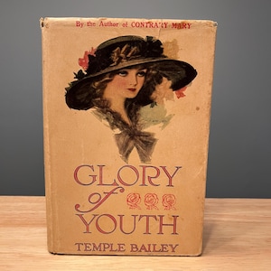 May include: Vintage book cover for "Glory of Youth" by Temple Bailey. The cover features an illustration of a woman wearing a hat, with the title in red script. The book is a light tan colour.