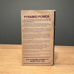 Op de afbeelding: Een rechthoekige boekomslag met de titel PYRAMID POWER in donkerbruine tekst op een cr&egrave;mekleurige achtergrond. De omslag bevat meerdere alinea's met promotionele tekst, waaronder citaten uit TIME Magazine, Daily News en Newsday, eindigend met de zin PUT PYRAMID POWER TO WORK FOR YOU!
