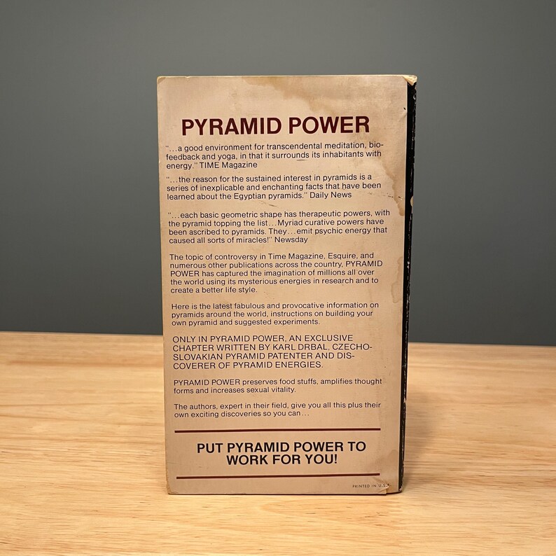 Op de afbeelding: Een rechthoekige boekomslag met de titel PYRAMID POWER in donkerbruine tekst op een cr&egrave;mekleurige achtergrond. De omslag bevat meerdere alinea's met promotionele tekst, waaronder citaten uit TIME Magazine, Daily News en Newsday, eindigend met de zin PUT PYRAMID POWER TO WORK FOR YOU!