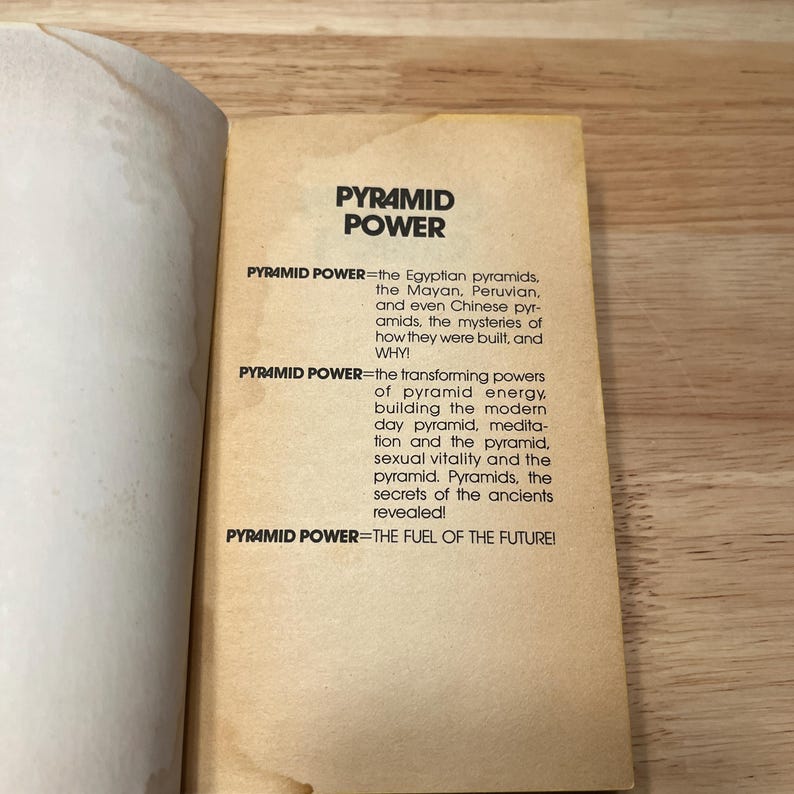 Op de afbeelding: Een bladzijde uit een boek met een lichtbruine achtergrond en zwarte tekst. De titel luidt PYRAMID POWER. De tekst beschrijft Egyptische, Mayaanse, Peruaanse en Chinese piramides, de mysteries van hun bouw, piramide-energie en brandstof.