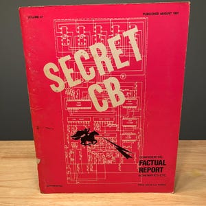 May include: A red book titled "SECRET CB" with white lettering and a schematic diagram. The cover includes the text "CONFIDENTIAL FACTUAL REPORT SCHEMATICS ETC." and "PUBLISHED AUGUST 1987". A black silhouette of a horse and rider is also visible.