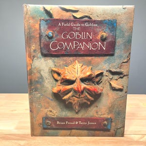 May include: A weathered book titled "A Field Guide to Goblins, The Goblin Companion." The cover features a sculpted goblin face and text on a textured, multi-colored background. Authors Brian Froud & Terry Jones are listed.