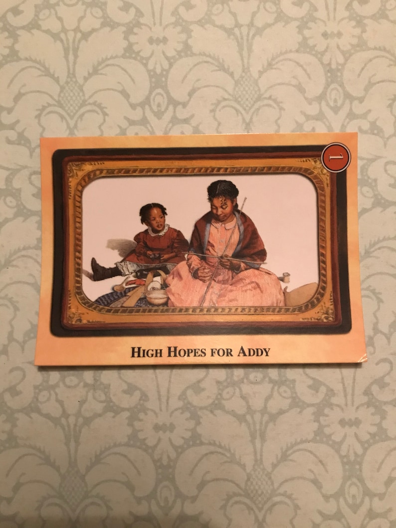 K&ouml;nnte beinhalten: Eine Illustration im Vintage-Stil mit zwei jungen schwarzen M&auml;dchen, eines sitzt, das andere steht, in einem gerahmten Bild. Das sitzende M&auml;dchen tr&auml;gt ein rosa Kleid und h&auml;lt eine Stricknadel. Das stehende M&auml;dchen tr&auml;gt ein rotes Kleid und h&auml;lt einen kleinen Gegenstand. Der Text "High Hopes for Addy" ist unter dem Bild gedruckt.