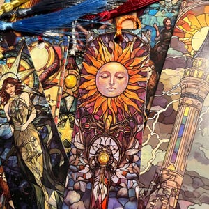 May include: A collection of colorful bookmarks with intricate stained-glass designs. The bookmarks feature images of a sun with a serene face, a woman, and a tower. Each bookmark has a tassel attached at the top.