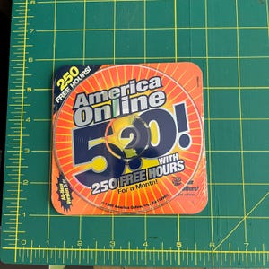 May include: A circular America Online 5.0 software disc on a square orange and yellow background. The text reads America Online 5.0! with 250 FREE HOURS. A measuring mat with yellow grid lines shows the disc is approximately 4.5 inches wide.