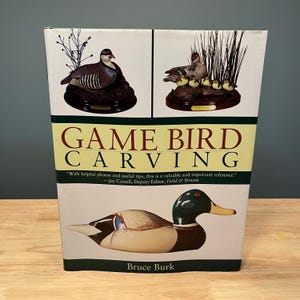May include: A book titled "Game Bird Carving" with images of carved birds. The cover features a carved duck and two smaller images of carved birds. The author's name, Bruce Burk, is at the bottom.