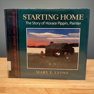 May include: A book titled "Starting Home: The Story of Horace Pippin, Painter" by Mary E. Lyons. The cover features an illustration of a log cabin with a person in front, set against a sunset. The book is part of the "African-American Artists and Artisans" series.