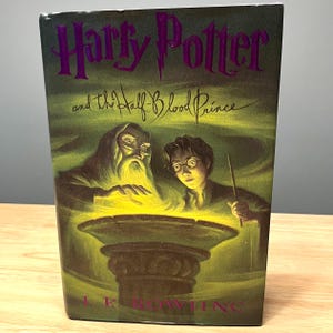 May include: A hardcover book titled "Harry Potter and the Half-Blood Prince" with a green and purple cover. The cover features illustrations of Dumbledore, Harry Potter, and a glowing bowl.