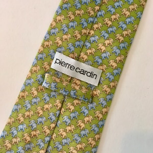 K&ouml;nnte beinhalten: Eine gr&uuml;ne Seidenkrawatte mit einem sich wiederholenden Muster aus hellblauen und beigen Elefanten. Die Krawatte hat ein wei&szlig;es Etikett mit dem Text "pierre cardin".