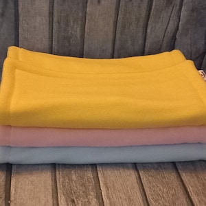 Könnte beinhalten: Ein Stapel aus drei Fleece-Decken in Gelb, Rosa und Hellblau.