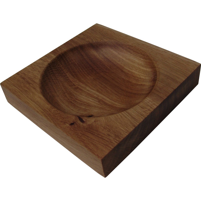 Puede incluir: Un cuenco de madera cuadrado con un centro redondeado y hundido. El cuenco est&aacute; hecho de madera marr&oacute;n oscura y tiene un acabado natural y r&uacute;stico.
