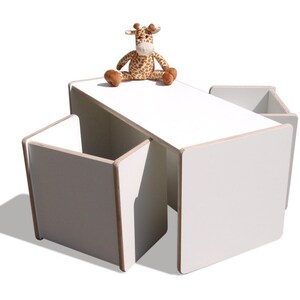 May include: White children's table and four chairs set. The table and chairs are made of wood and have a white finish. A stuffed giraffe toy is sitting on the table.