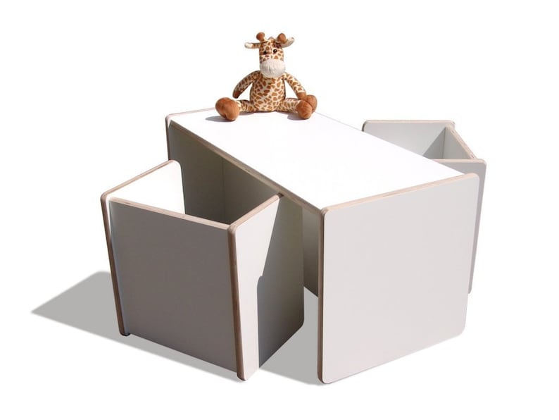 May include: White children's table and four chairs set. The table and chairs are made of wood and have a white finish. A stuffed giraffe toy is sitting on the table.