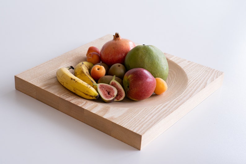 Puede incluir: Un cuenco de madera lleno de una variedad de frutas, incluyendo pl&aacute;tanos, higos, manzanas, mangos y granadas.