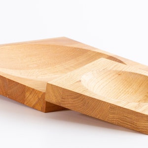 Puede incluir: Dos cuencos de madera, uno m&aacute;s grande que el otro, est&aacute;n anidados. Ambos cuencos est&aacute;n hechos de madera de color claro y tienen una forma redondeada ligeramente c&oacute;ncava.