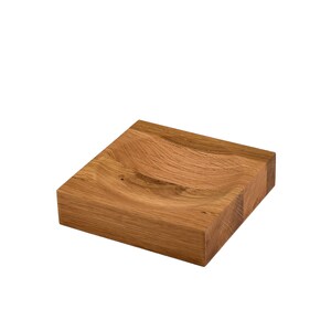 Puede incluir: Un plato cuadrado de madera con una hendidura curva en el centro. El plato est&aacute; hecho de madera marr&oacute;n claro y tiene un acabado natural.