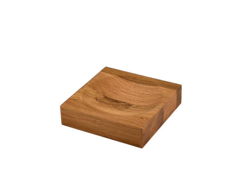Puede incluir: Un plato cuadrado de madera con una hendidura curva en el centro. El plato est&aacute; hecho de madera marr&oacute;n claro y tiene un acabado natural.