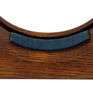 Könnte beinhalten: Ein Holzständer mit einer gekrümmten, gepolsterten Oberseite zum Ausstellen einer Schallplatte. Der Ständer ist aus dunkelbraunem Holz gefertigt und hat eine natürliche Oberfläche.