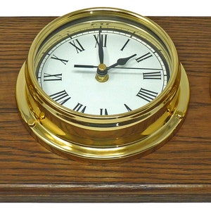 Könnte beinhalten: Ein Holzsockel trägt drei Instrumente mit Messingrahmen: einen Gezeitenanzeiger, eine Uhr mit römischen Ziffern und ein Barometer. Die Uhr zeigt 12:00 Uhr an. Die Instrumente haben weiße Zifferblätter und schwarze Zeiger.