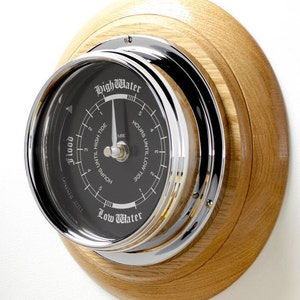 Può includere: Un orologio a marea cromato e nero con cornice in legno. Il quadrante dell'orologio ha le parole "High Water" e "Low Water" stampate su di esso. Il quadrante dell'orologio ha anche un ago che punta al livello di marea attuale.