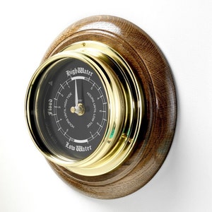 May include: A brass and wood tide clock with a black face. The clock has markings for hours until high tide and hours until low tide. The clock face also has the words "High Water" and "Low Water" printed on it.