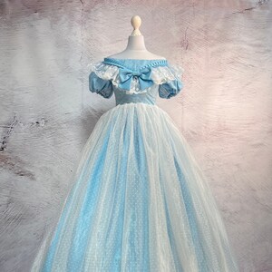 May include: A light blue ball gown with a white lace bodice and a white tulle skirt with polka dots. The dress has a large blue bow at the neckline and a white satin ribbon trim at the hem.