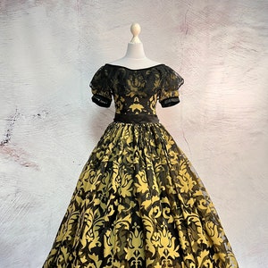 May include: A black and gold ball gown with a damask pattern. The dress has a fitted bodice with a black lace overlay and a full skirt.