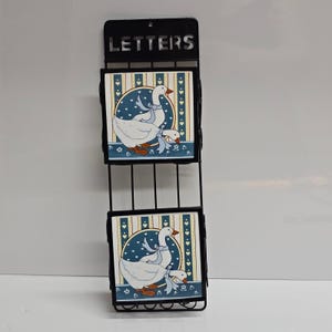 May include: A black metal wall-mounted letter holder featuring two square tiles. Each tile displays a white goose with a blue ribbon against a blue and cream striped background with small heart motifs. The top of the frame has the word LETTERS cut out.